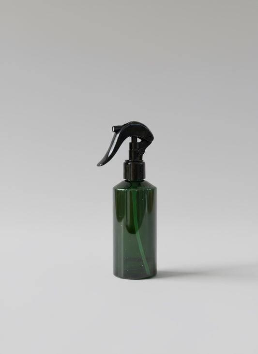 Green spray bottle with black nozzle on a wooden surface with cardboard box in the background
